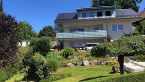 A two-story house with a balcony, surrounded by a well-maintained garden with various plants and a lawn. - Apartment 'Fewo Zeit Zu Zweit' with Mountain View, Private Terrace and Wi-Fi (Sasbachwalden)