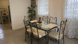 Comedor con mesa de vidrio y sillas metálicas, unidad de aire acondicionado y ventilador de techo.