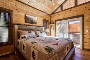 A wooden cabin bedroom with a bed, a painting, and a view of the outside.