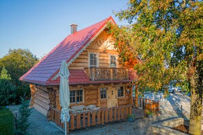 A wooden cabin with a red roof, a balcony, and a small porch area.