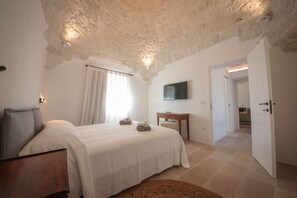A bedroom with a bed, a bedside table, a flat-screen TV mounted on the wall, and a door leading to another room. - TD Trulli Lorusso Design Luxury Trulli With Pool (Castellana Grotte)