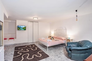 Un dormitorio con una cama, un televisor, una silla y una alfombra decorativa.
