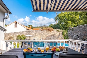En terrasse med et spisebord dækket til morgenmad, med udsigt til en pool og en stenvæg.