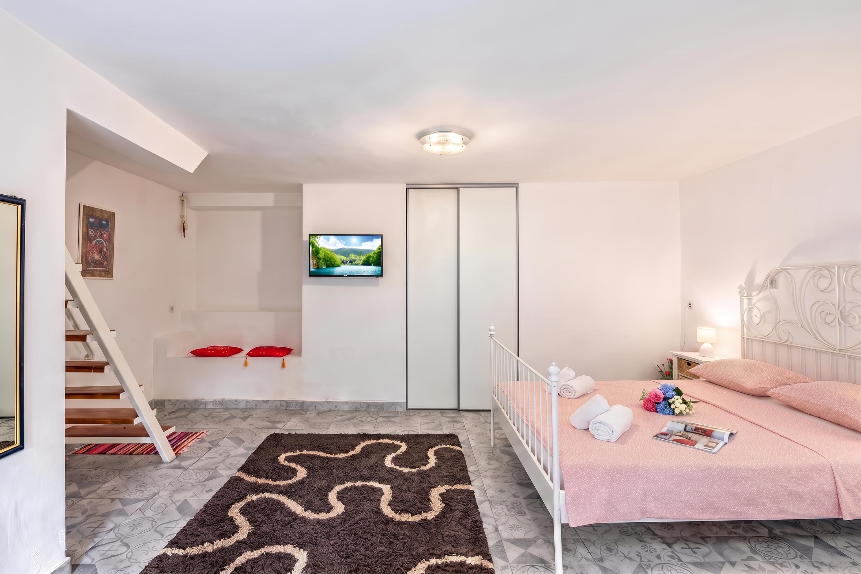 A bedroom with a bed, a TV, a wardrobe, and a staircase.
