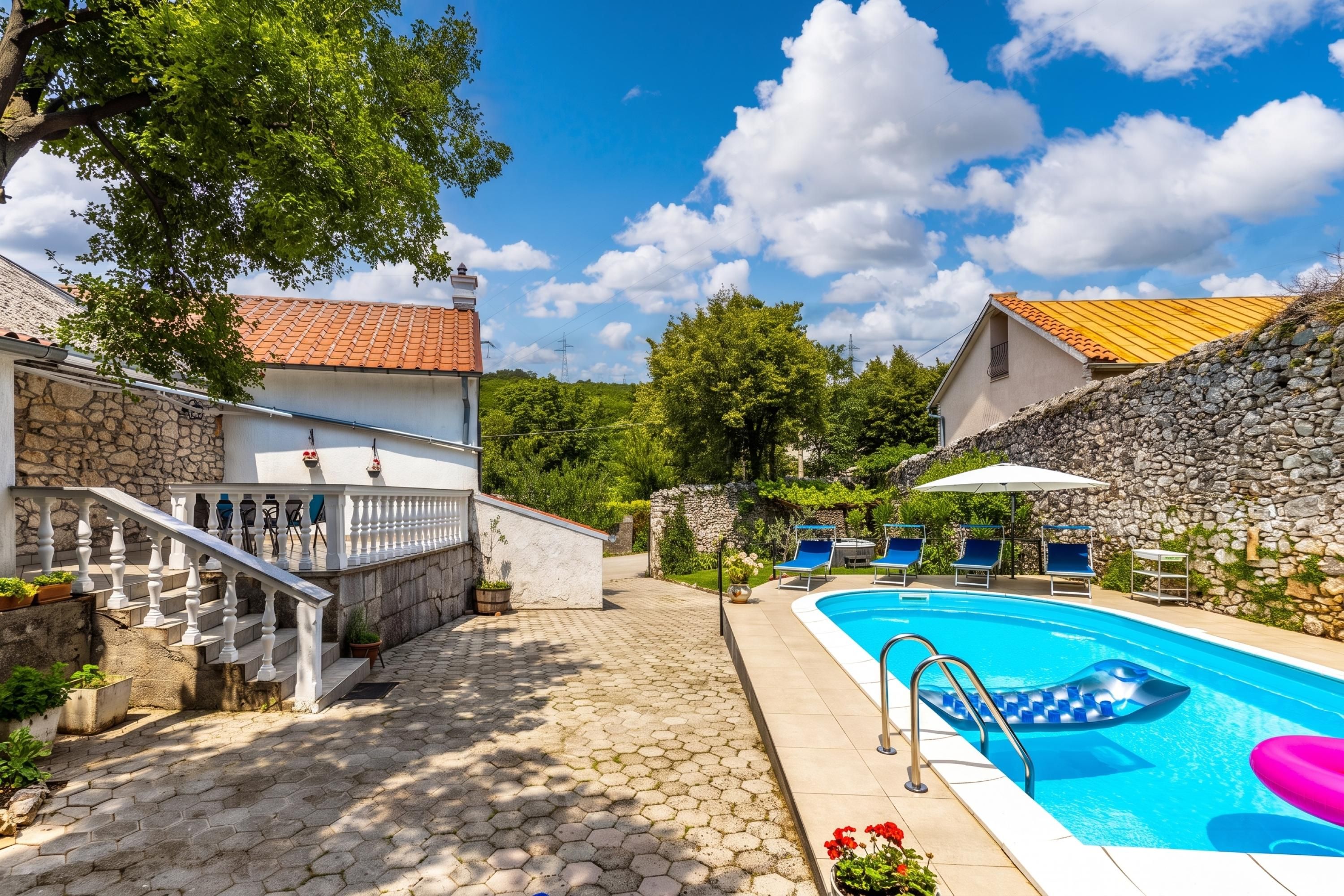 A swimming pool with a stone wall and a staircase leading to a building with a tiled roof.