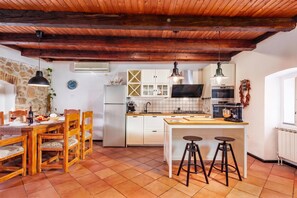 Cozinha com teto de madeira, armários brancos, uma ilha central com banquetas e uma área de jantar com mesa e cadeiras.