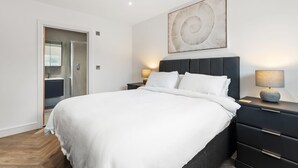 A modern bedroom with a large bed, a dark headboard, bedside lamps, and a wall-mounted abstract art piece. - The Paddock - Lovely Cottage With Hot Tub (Tenby)