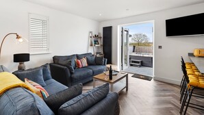 A modern living room with a sofa, coffee table, and a TV. There is a sliding door leading to an outdoor area. - The Paddock - Lovely Cottage With Hot Tub (Tenby)