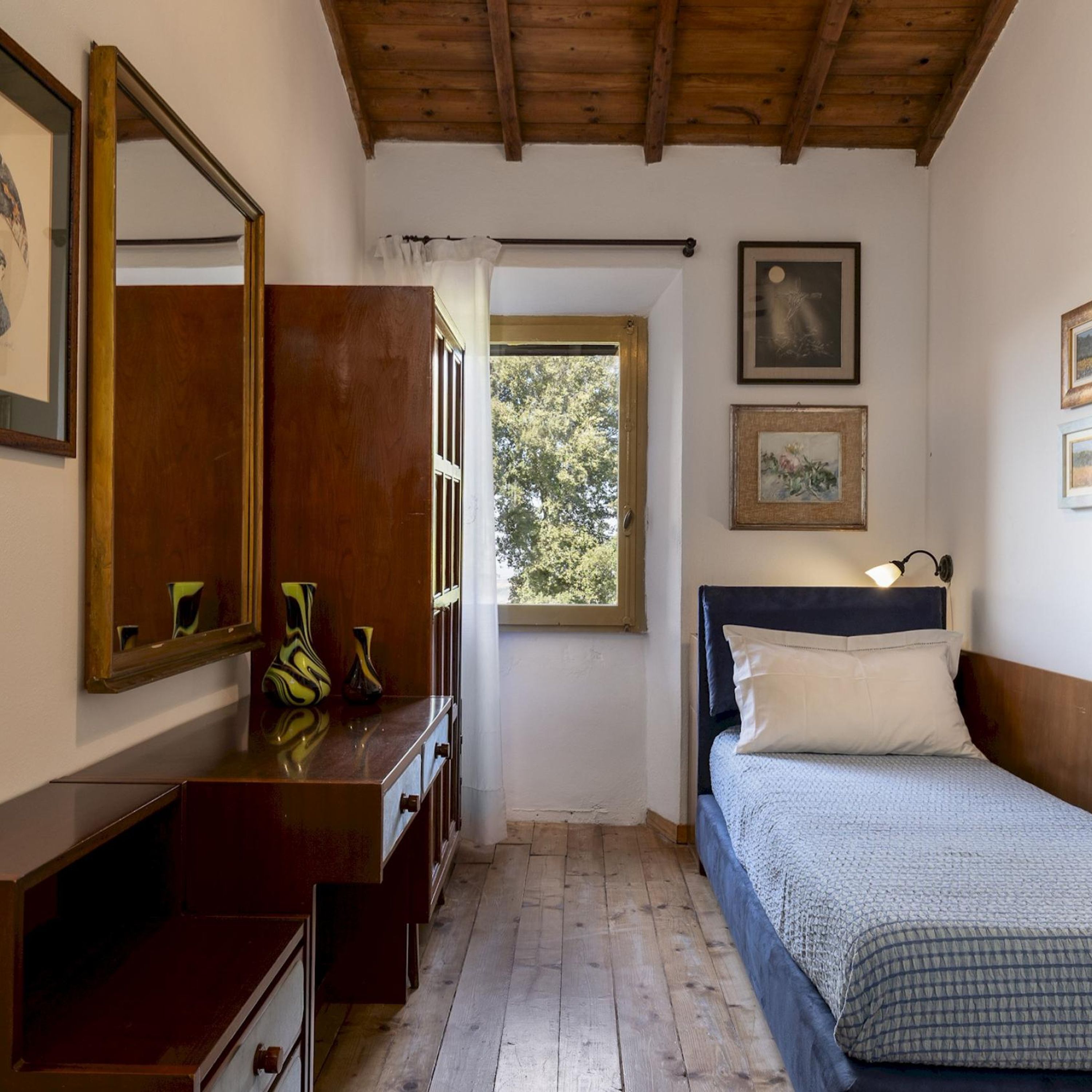 A bedroom with a wooden ceiling, a bed with a headboard, a dresser, a mirror, and two framed pictures on the wall.