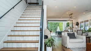 Una escalera con baldosas estampadas y escalones de madera que conduce a una sala de estar con un sofá, una planta en maceta y vistas al exterior.