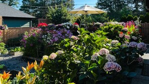 Ein Garten mit verschiedenen Blumen und Pflanzen, einem Holzzaun und einem Haus im Hintergrund.
