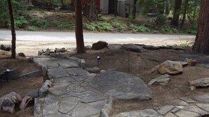 Un sendero de piedra en un área boscosa con árboles y una carretera al fondo.