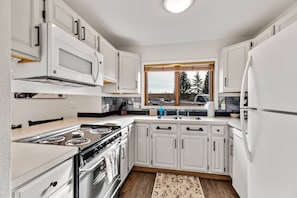 Una cocina moderna con armarios blancos, una estufa de acero inoxidable y una ventana con vistas a árboles.