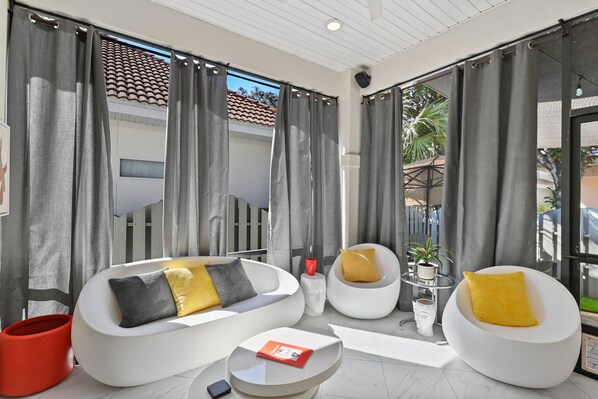 A modern living room with a white sofa, yellow and gray cushions, a red ottoman, and a glass coffee table.