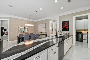 A modern kitchen with a black marble countertop, white cabinets, and a dining area with a chandelier.