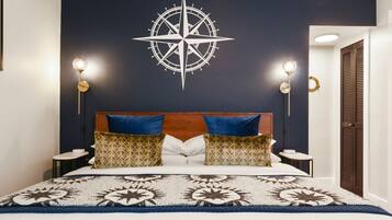 A neatly made bed with a patterned bedspread, two blue pillows, and a decorative compass on the wall.