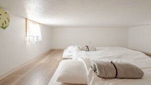Un dormitorio con piso de madera, una cama con ropa blanca y una ventana con cortinas blancas.