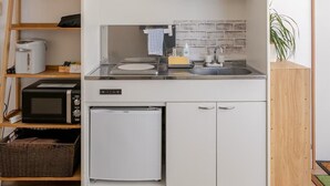 Cocina compacta con microondas, tostadora y refrigerador. Hay repisas sobre la encimera con tazas y una planta a la derecha.
