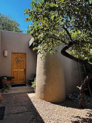 A courtyard with a wooden door, a large column, and a tree.