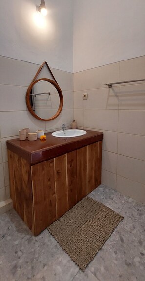 Sink and round mirror above a tiled wall, with a towel rack and small rug.