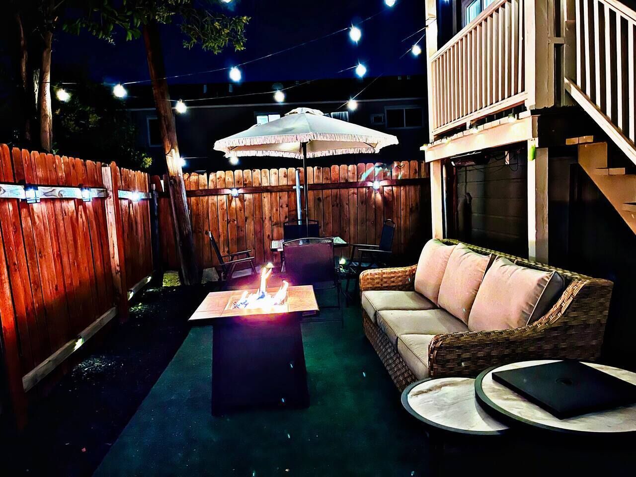 Ein Außenbereich mit Terrasse, einem Feuerelement, einem Korbsessel-Sofa und einem Esstisch.