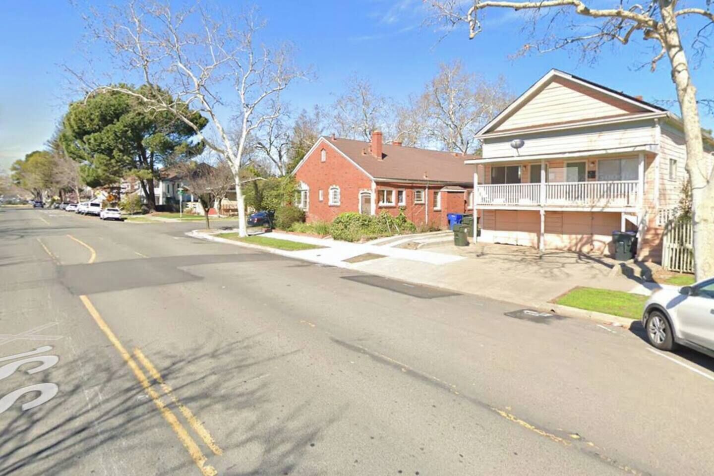 A residential street with houses, a clear sky, and a parked car.