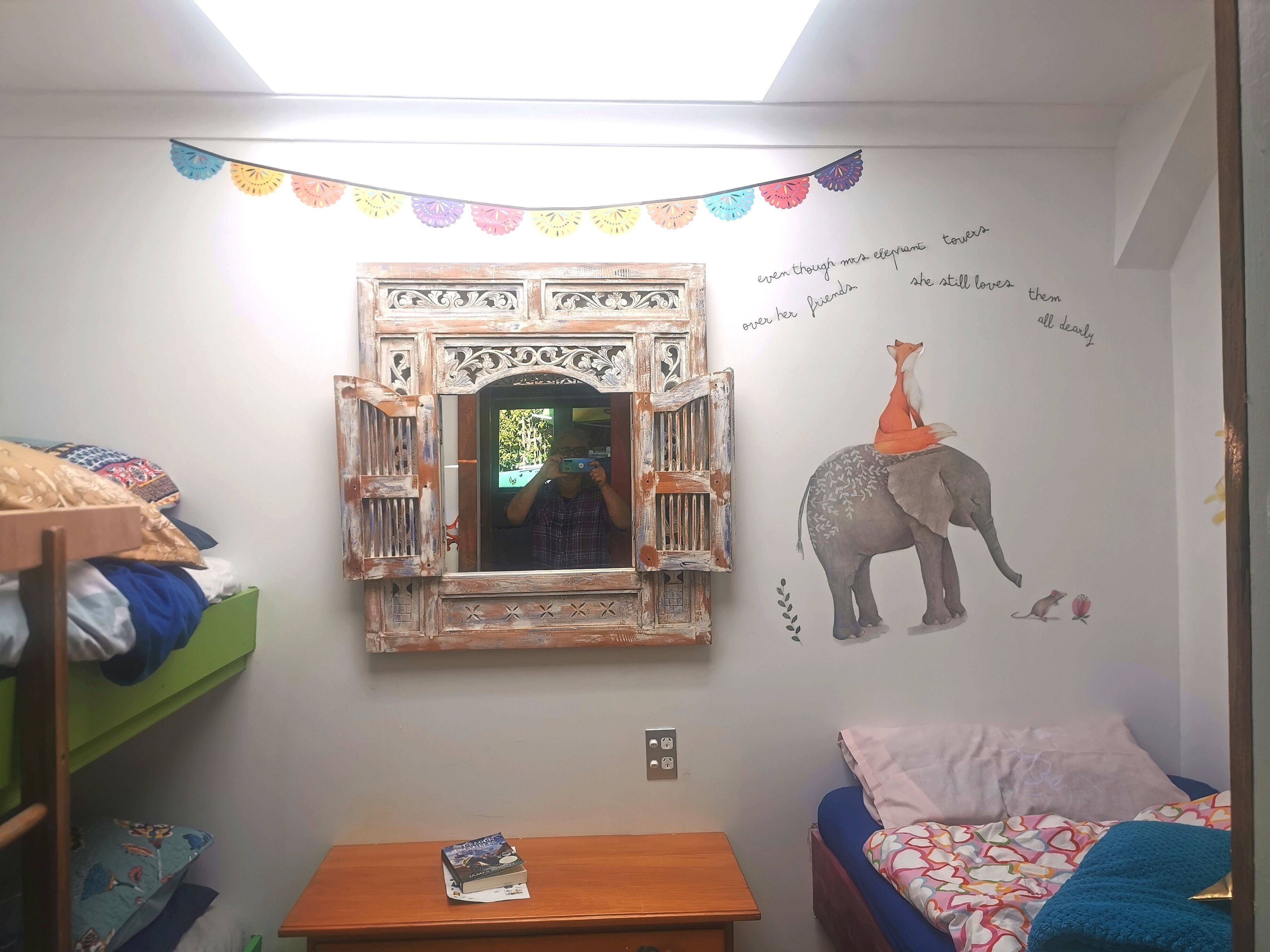 A child's bedroom with a bunk bed, a small table with a book, a decorative mirror, and a wall mural of an elephant and a fox.