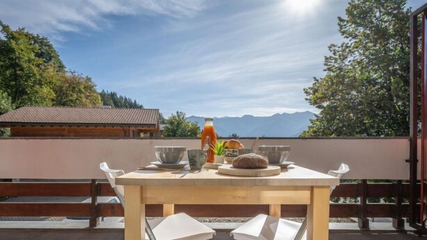 A wooden table with a view of mountains, a glass of juice, and a loaf of bread on a balcony. - Beau séjour 15 by Interhome (Ovronnaz)