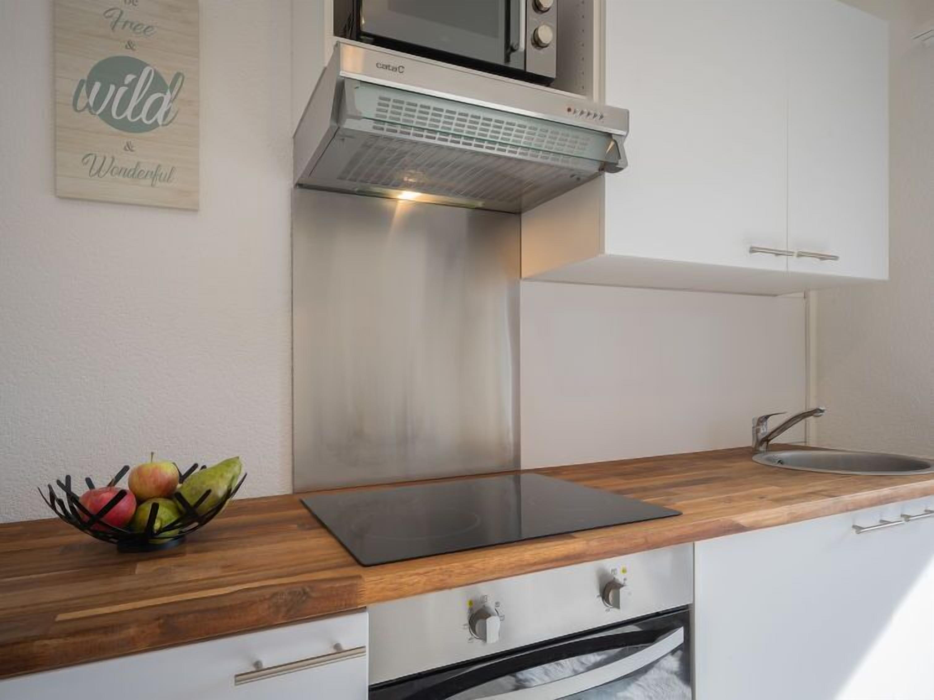 Una cocina moderna con extractor acero inoxidable, microondas y fregadero.