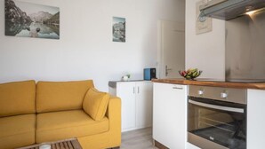 A compact living space with a sofa, kitchenette, and two framed pictures on the wall. - Beau séjour 15 by Interhome (Ovronnaz)
