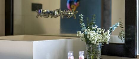 A bathroom with a bathtub, a mirror, and a tray with two bottles and a vase of flowers.