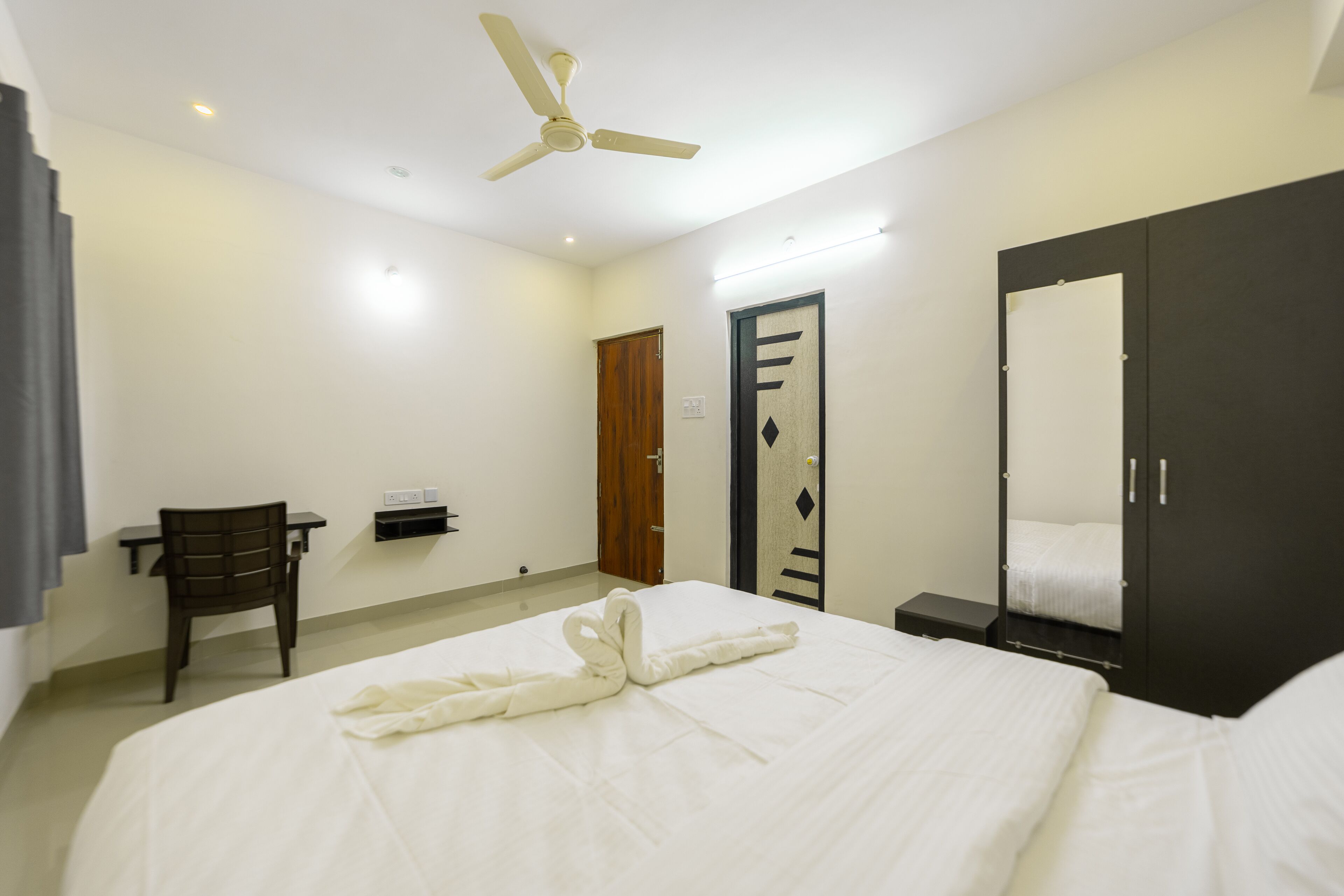 A hotel room with a bed, a desk, a chair, a wardrobe, and a ceiling fan.