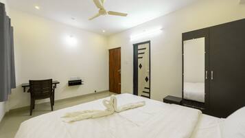 Una habitación de hotel con cama, escritorio, silla, armario y ventilador de techo.