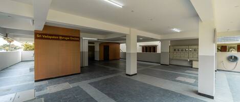 A spacious lobby with a sign for Sri Vadapalani Murugar Enclave, a reception desk, and a row of lockers.