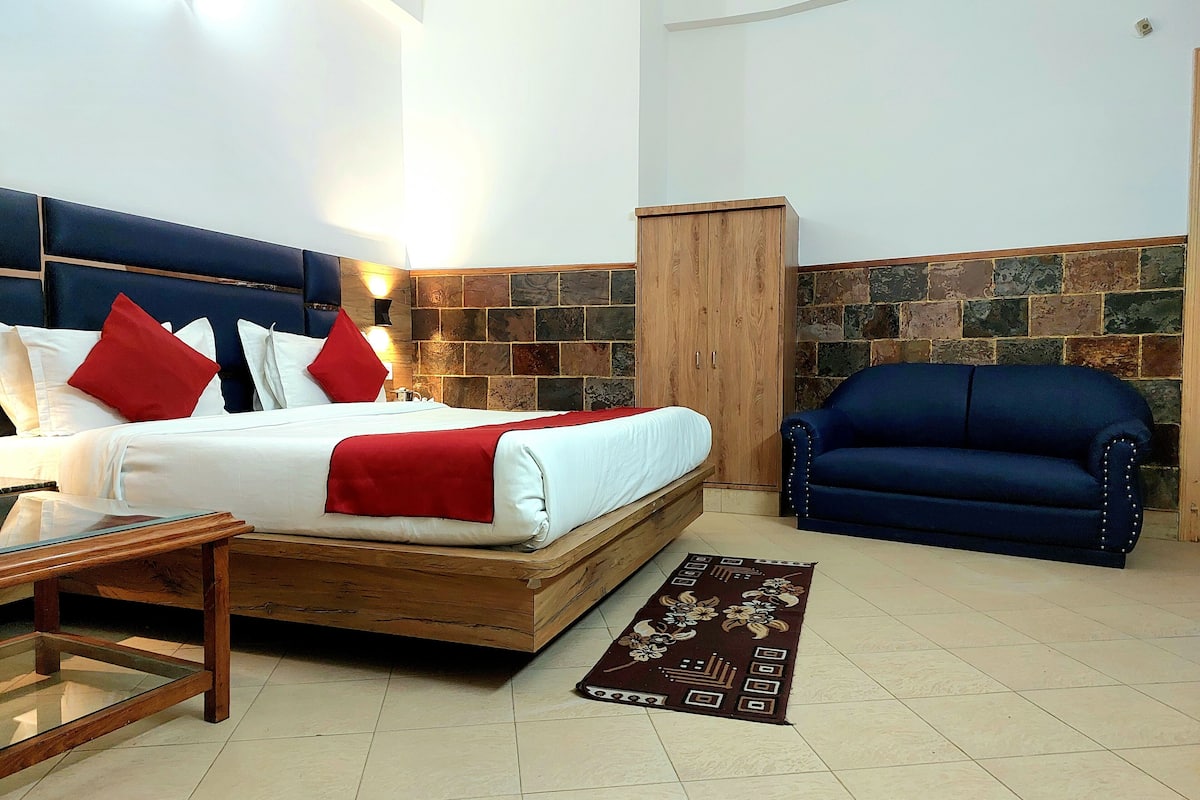 A bedroom with a bed, a wooden wardrobe, a blue sofa, and a patterned rug.