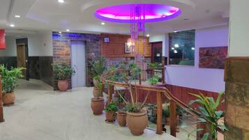 A hotel lobby with a central staircase, potted plants, and a modern ceiling design.