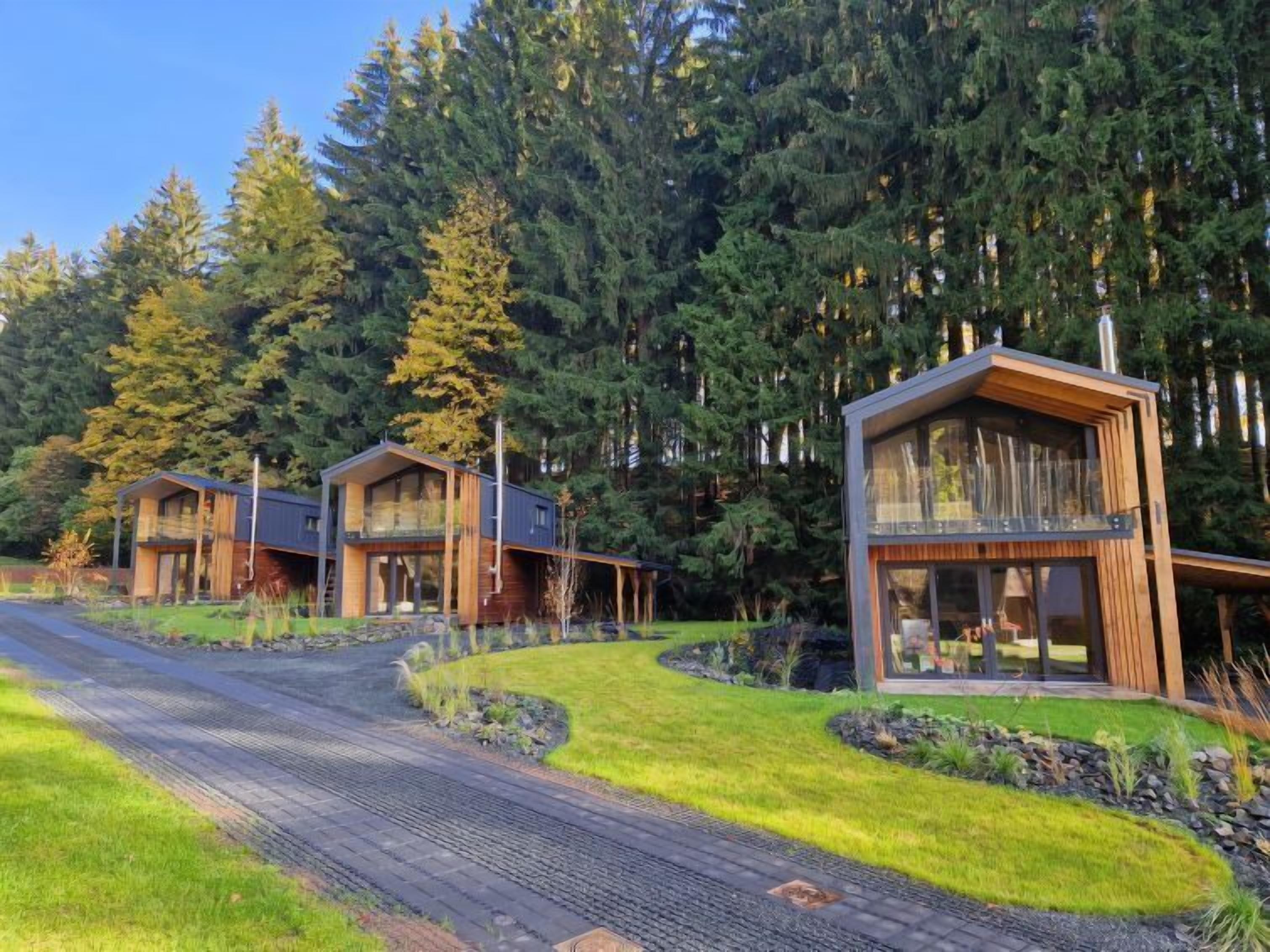 A modern cabin-style building with a glass balcony, surrounded by a forested area.