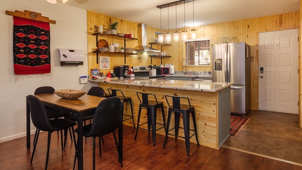 A kitchen with wooden walls, a central island with bar stools, a refrigerator, and a coffee machine. - Latitude Adjustment by Velo (Angel Fire)