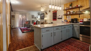 A kitchen with light blue cabinets, a marble countertop, hanging pendant lights, and a red patterned rug. - Latitude Adjustment by Velo (Angel Fire)