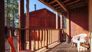 A wooden deck with a covered area, two chairs, and a red chair. - Latitude Adjustment by Velo (Angel Fire)