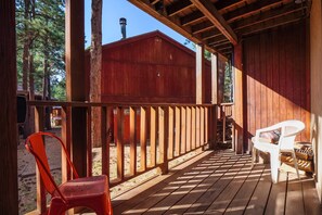 Una terraza de madera con barandilla, una silla roja y una silla blanca.