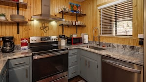A kitchen with granite countertops, stainless steel appliances, wooden panel walls, and a window with blinds. - Latitude Adjustment by Velo (Angel Fire)