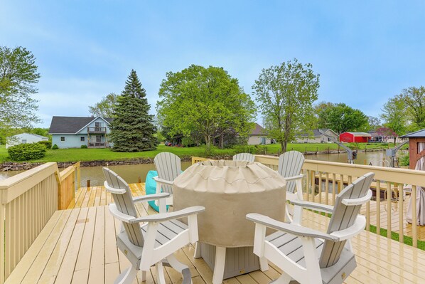 Relax on the deck with a round table and four Adirondack chairs overlooking a serene body of water.