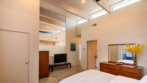 Een slaapkamer met een bed, een televisie, een dressoir en een spiegel.