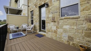Une terrasse en bois avec des meubles d’extérieur, des murs en pierre et de grandes fenêtres.