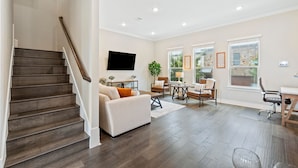 Un salon spacieux avec un escalier, un téléviseur à écran plat, un coin repas et de grandes fenêtres.