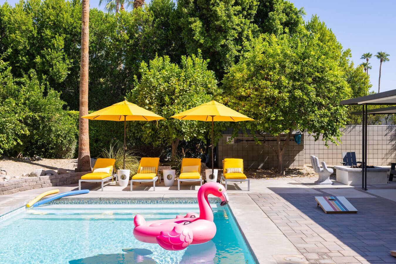 A swimming pool with a pink flamingo float, yellow umbrellas, and sun loungers.