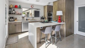 Uma cozinha moderna com ilha central, banquetas, micro-ondas e cafeteira.