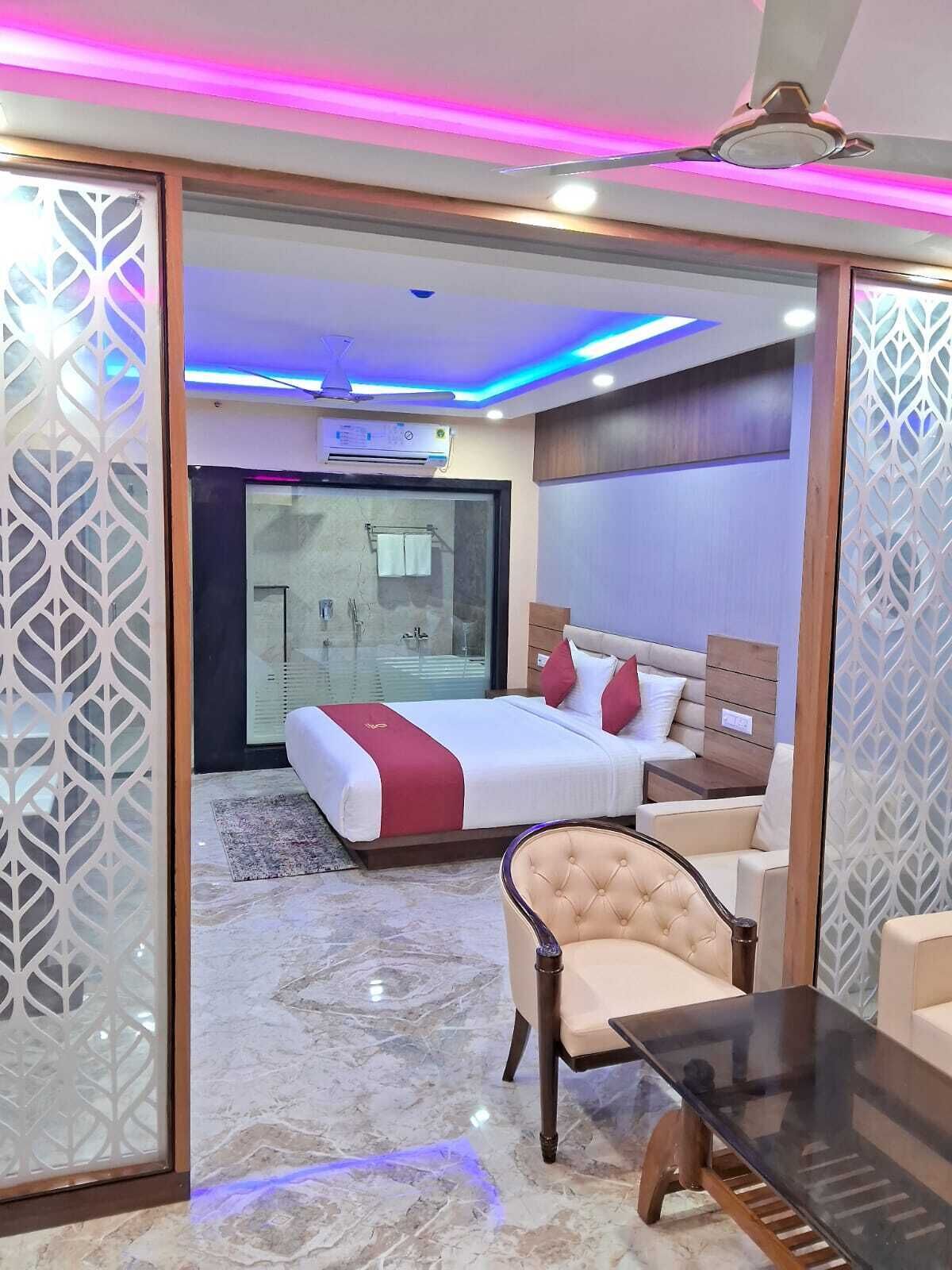 A modern hotel room with a bed, a seating area, and a glass partition.