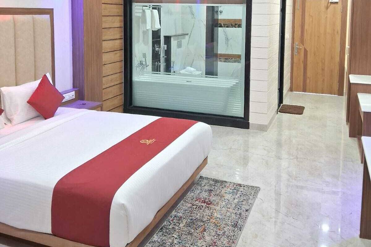 A modern hotel room with a large bed, a glass shower enclosure, a ceiling fan, and an air conditioning unit.